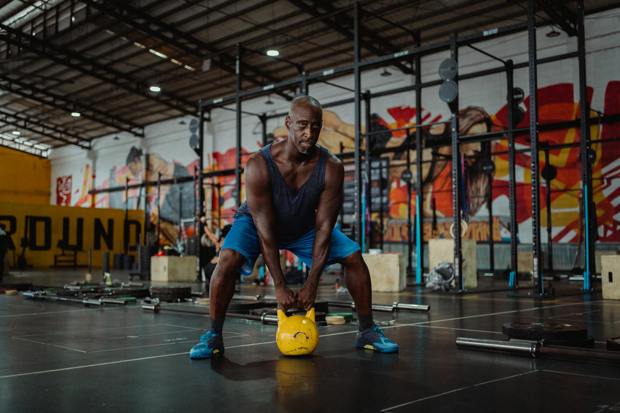 Strong African American man working out indoors, lifting a kettlebell in a modern gym.